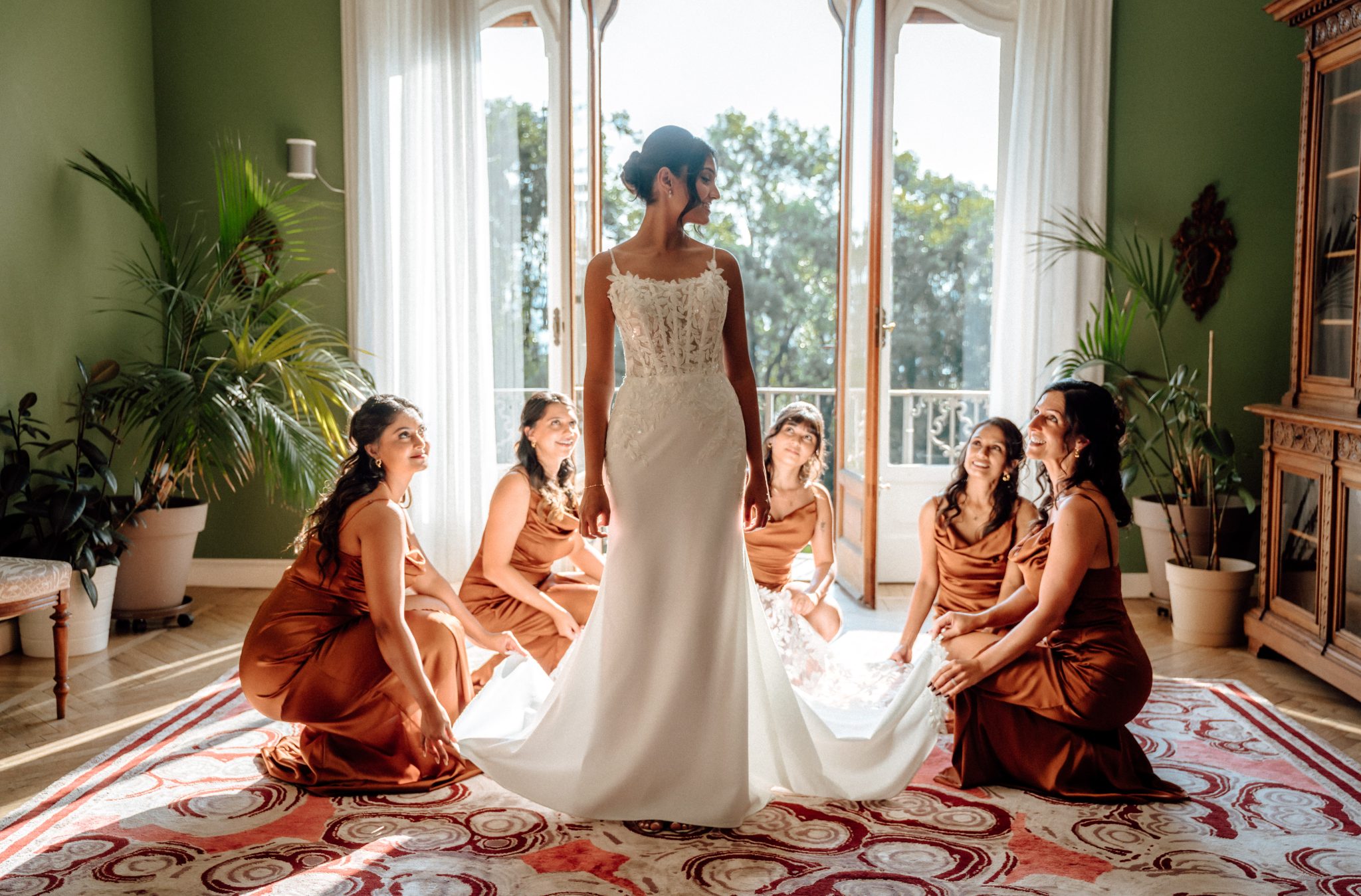 Bride standing among her bridesmaids in orange dresses in a green room