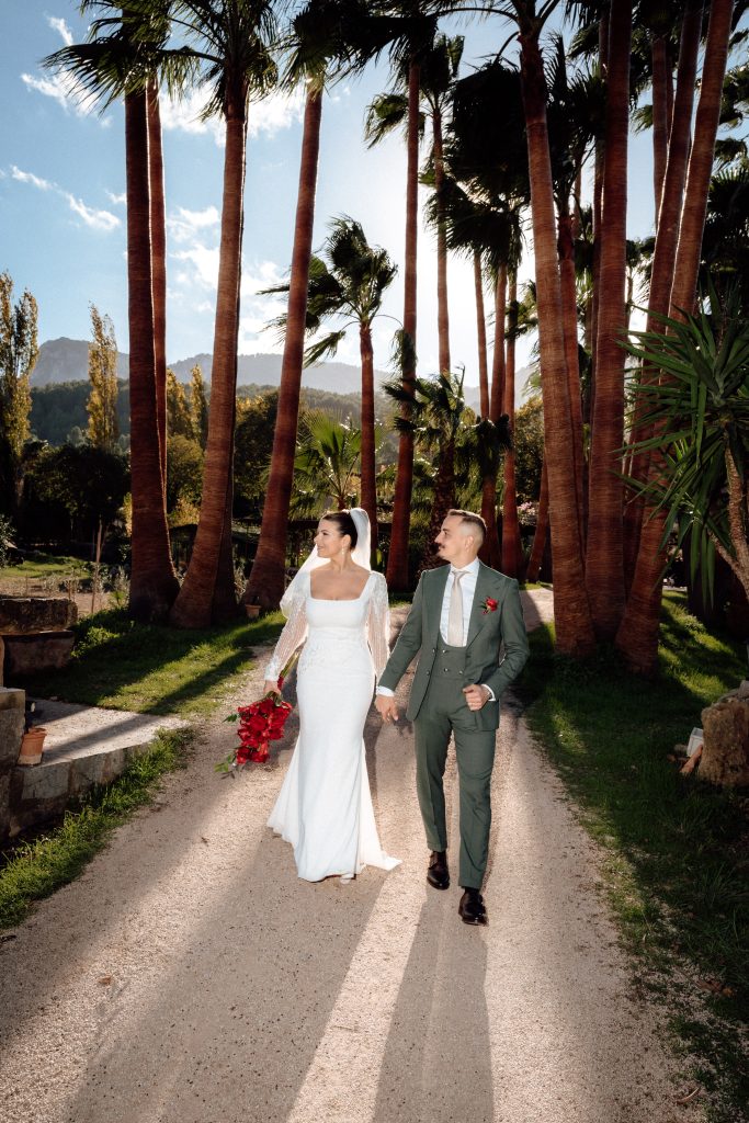 Bride and groom walking along a path between tall palm trees