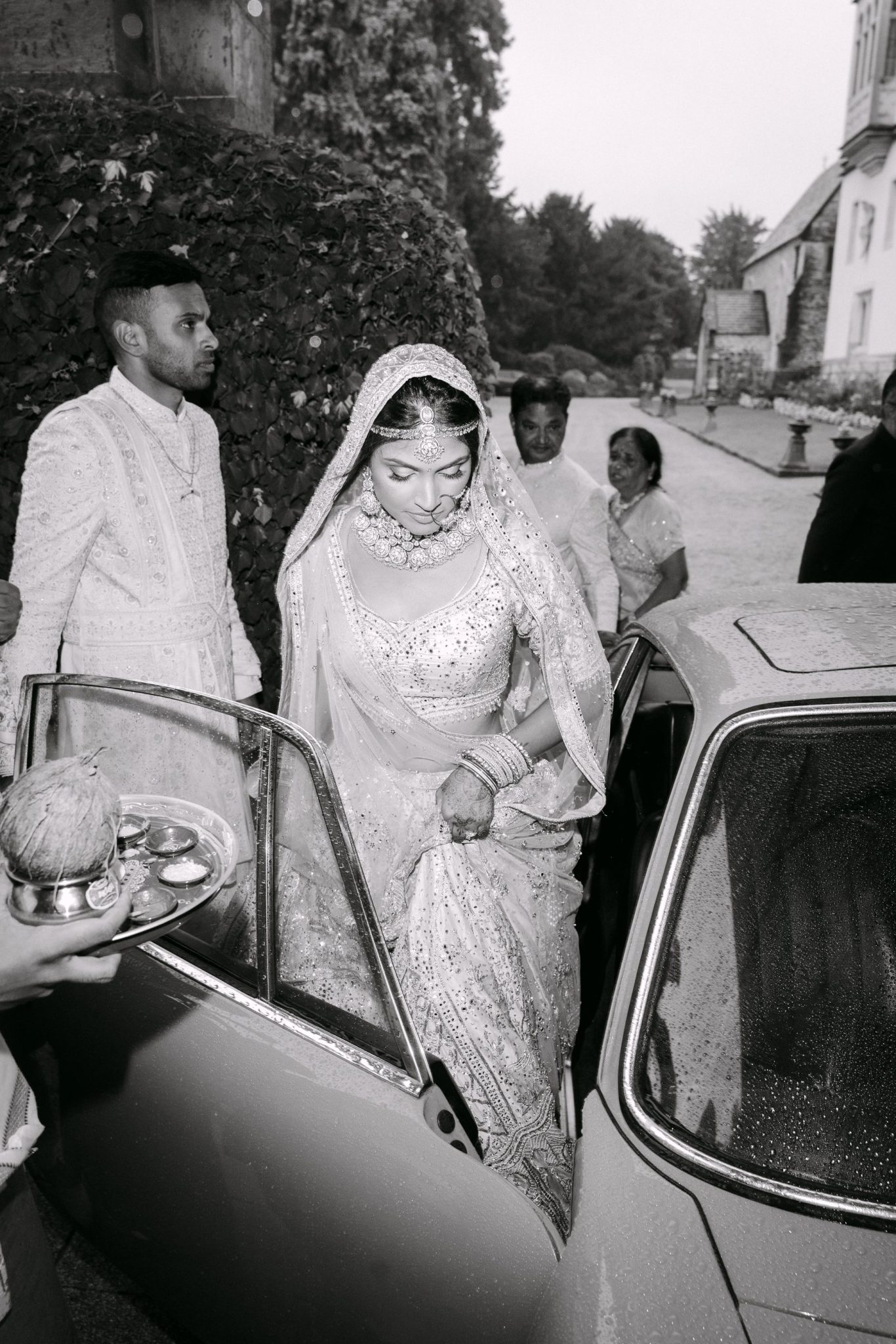Indian bride in a lehenga stepping out of a vintage car, black and white