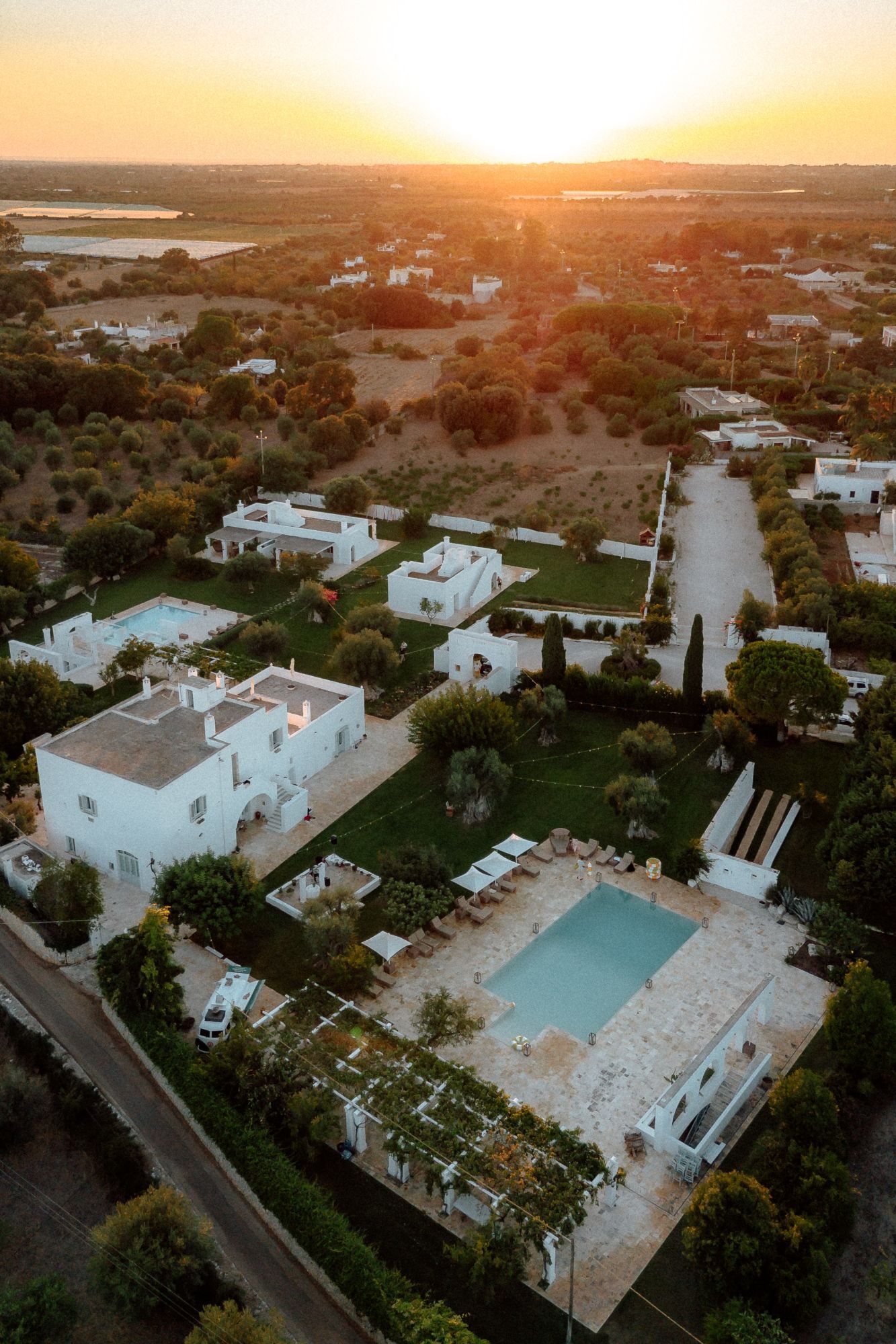 Aerial view of a white wedding estate with a pool and olive trees at sunset