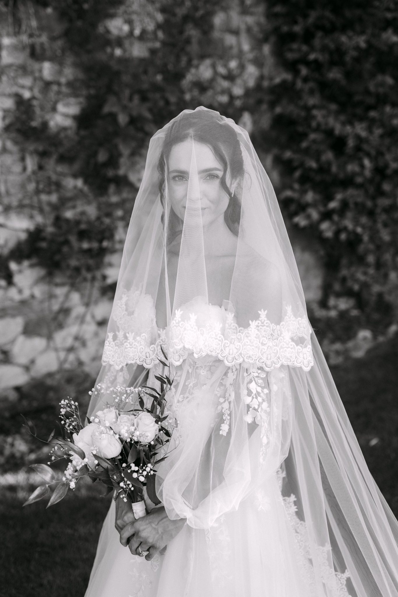 Bride in a long lace veil holding a bouquet, black and white portrait