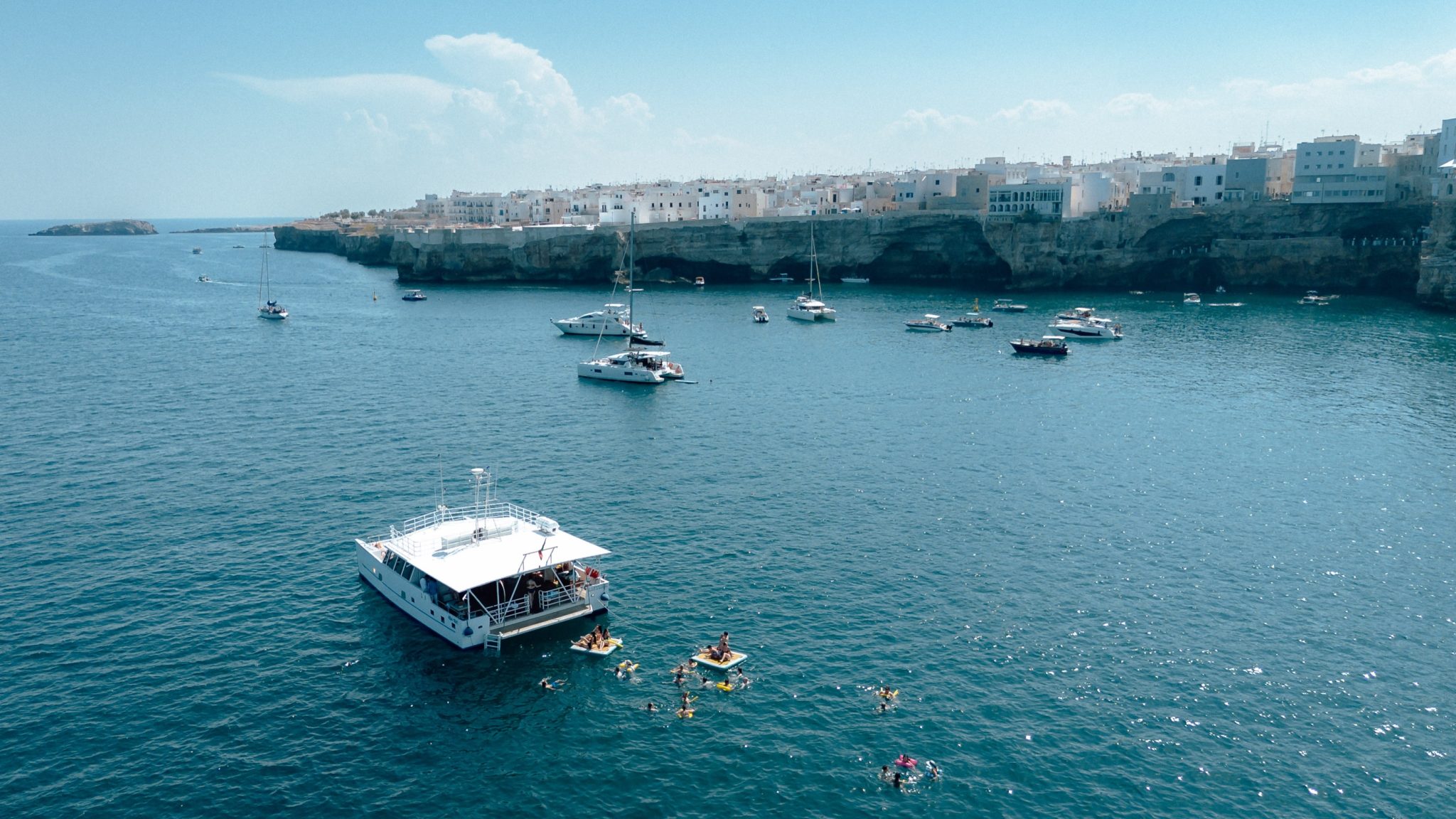 Aerial view of the cliffs and old town of Polignano a Mare with boats on the sea