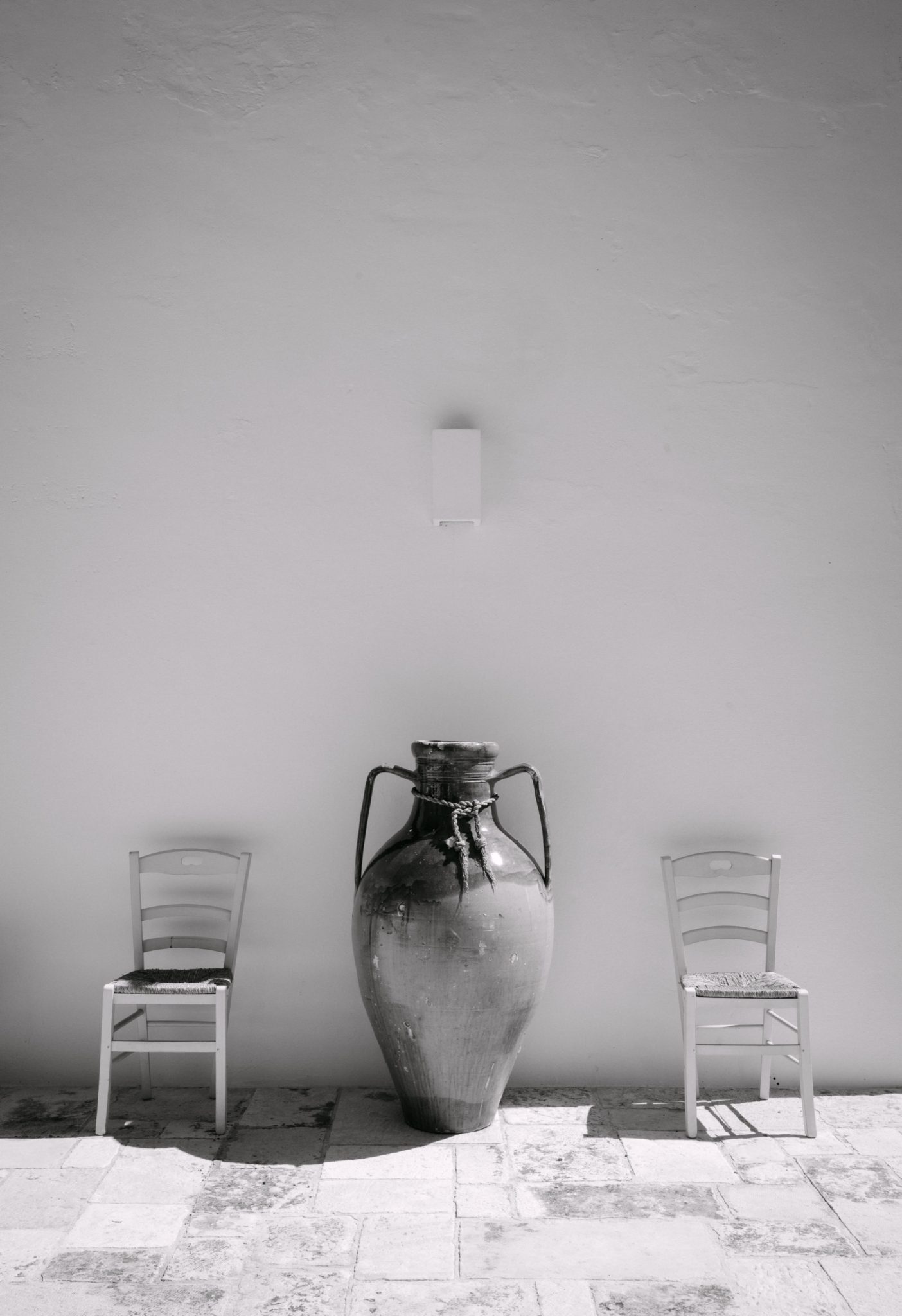 Black and white clay amphora and two chairs against a white wall