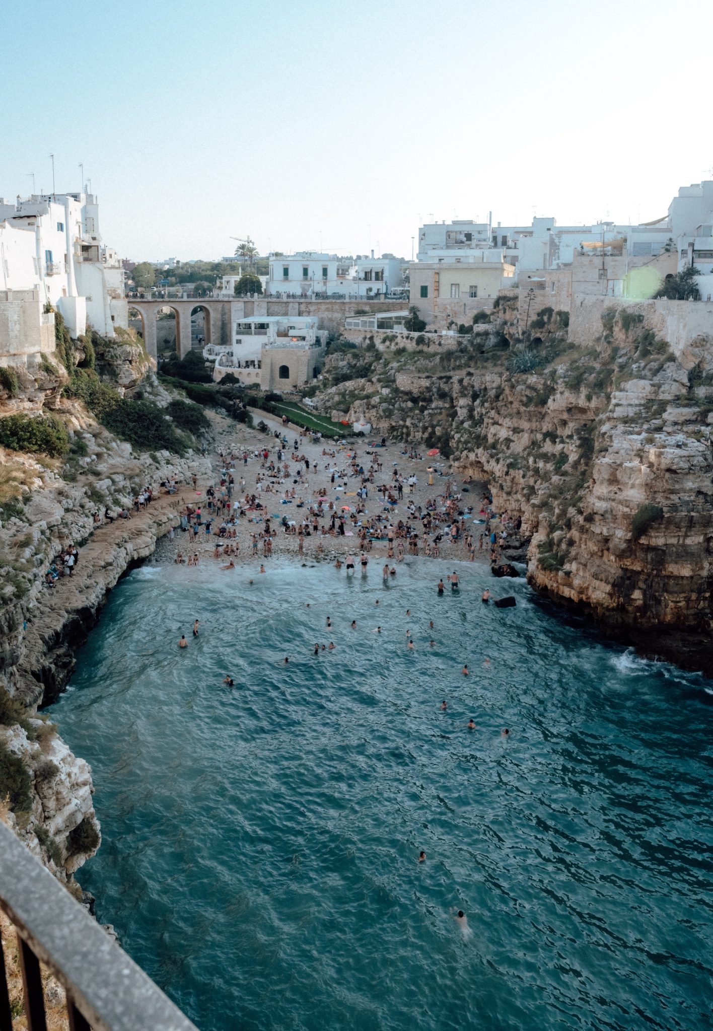 Rocky cove with swimmers and an old bridge in Polignano a Mare