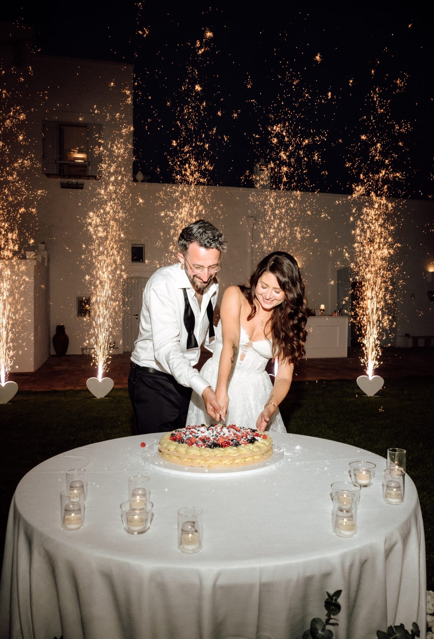 Bride and groom cutting their wedding cake with sparklers at night