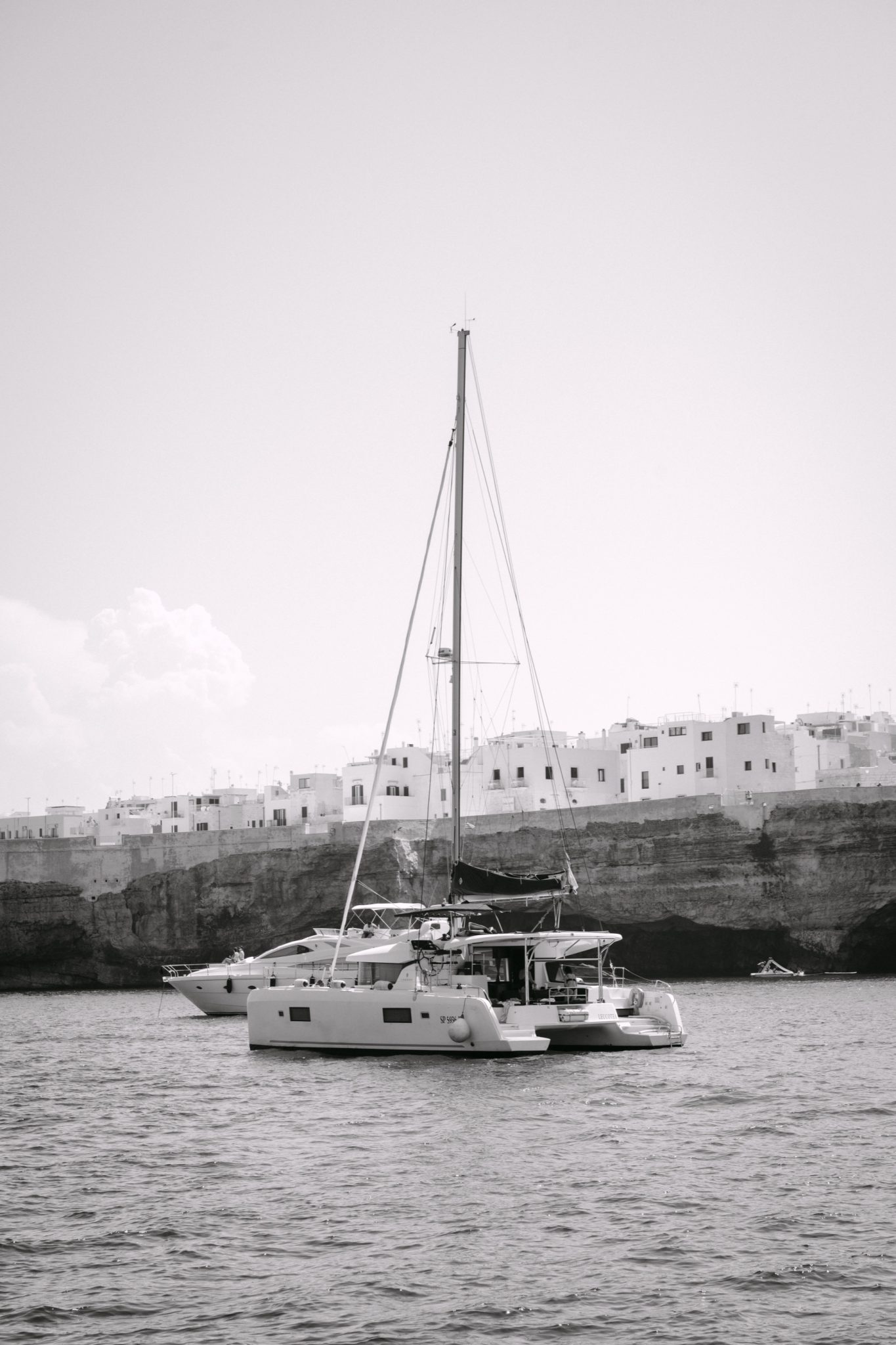 Black and white sailboat in front of the cliffs of Polignano a Mare